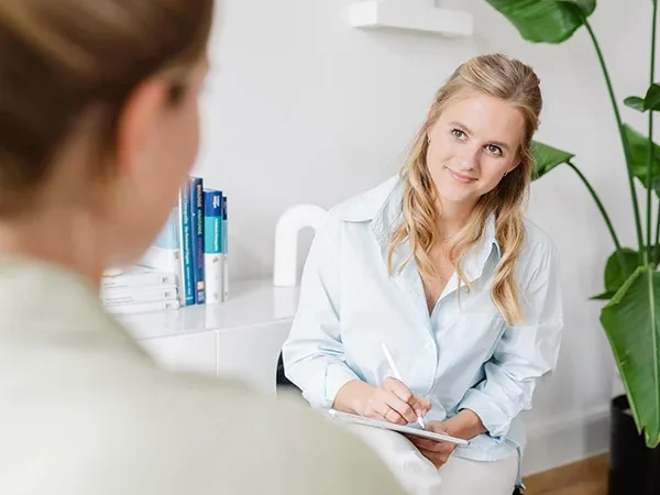 Die Osteopathin lächelt und macht sich Notizen während des Patientengesprächs in der Praxis Heck Osteopathie Düsseldorf.